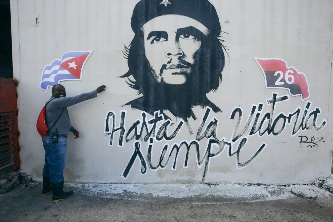 man posing by wall with che guevara mural
