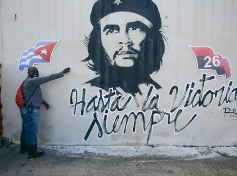 man posing by wall with che guevara mural